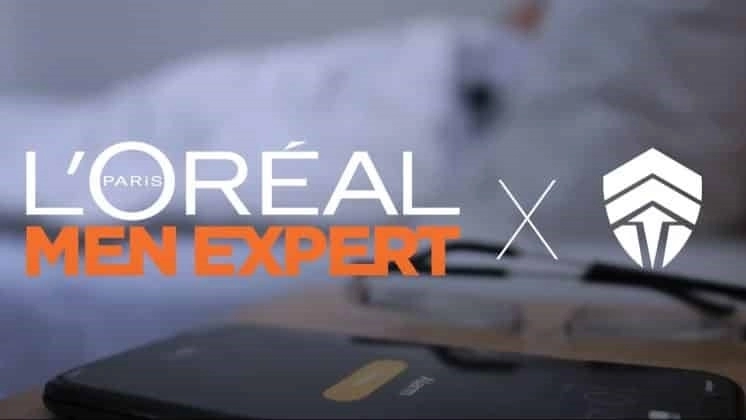 Смартфон лежит на тумбочке, на экране виден будильник.  Слова L'Oréal Paris Men Expert появляются над ним рядом с логотипом Chiefs Esports Club.