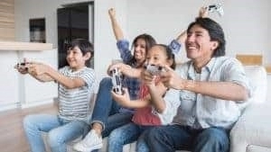 A family of gamers sit on the couch with controllers in hand, enjoying a game together