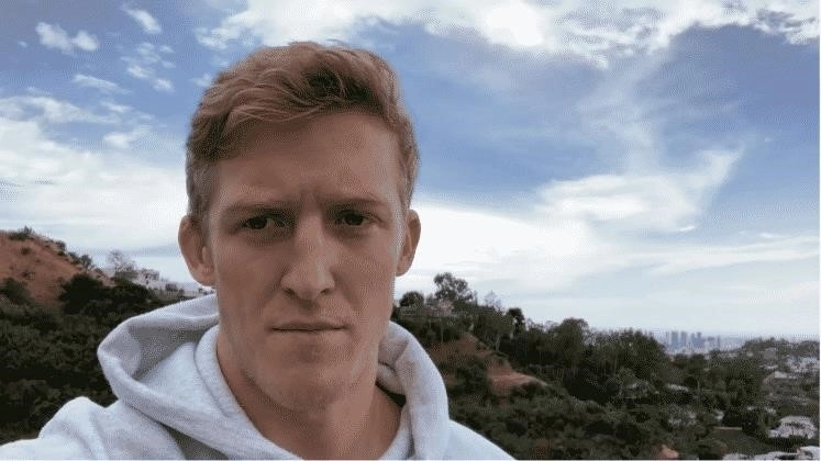 Тернер «Tfue» Тенни стоит на фоне голубого неба с серьезным выражением лица, глядя в камеру.