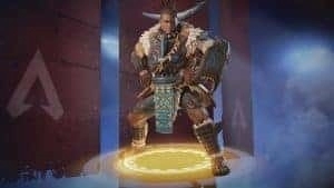 Apex Legends legend Gibraltar is shown wearing a legendary edition outfit made from animal skins and looks tribalistc. He stands on a yellow glowing circle and has three flags behind him showing the Apex Legends triangle logo in a blue mist