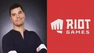 Генеральный директор Riot Games Николо Лоран улыбается, сложив руки рядом с логотипом Riot Games с кулаком на красном фоне.