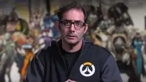 Jeff Kaplan talks to the camera with the cast of Overwatch characters in a mural behind him.