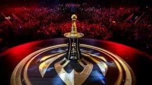 Приз LoL Mid-Season Invitational находится на подиуме на сцене перед большой толпой, освещенной красными огнями.