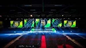 An empty arena venue is lit up with spotlights and monitors above the stage are lit in green with the words 