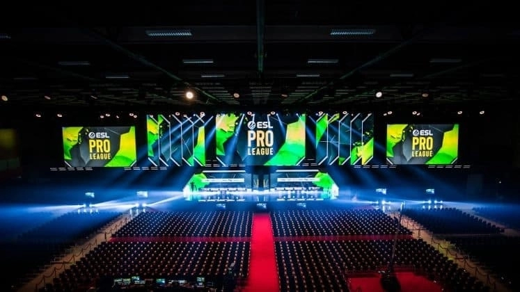 An empty arena venue is lit up with spotlights and monitors above the stage are lit in green with the words 