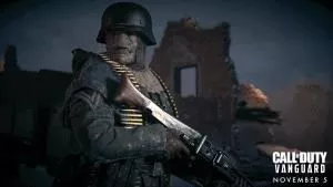 A heavily armored soldier holds a machine gun by a ruined building with the Call of Duty Vanguard logo in the corner.