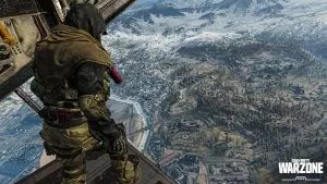 An operator stands at the rear paratrooper door of a plane, looking down at the trees and buildings below