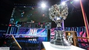 The League of Legends World Championship trophy is on the 2020 Worlds stage as the Finals match between DAMWON and Suning plays on in the background.