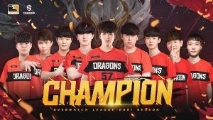 Полный состав Shanghai Dragons 2021 Overwatch League отображается вместе с трофеем на заднем плане позади них и золотыми словами «Чемпион» впереди.