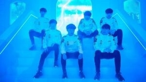 The roster for DAMWON KIA sit on white stairs with an arch window behind them showing a neon blue sky.