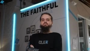 Jonathon McDaniels poses with his arms folded and a CLG shirt on, beneath writing on a wall that say 