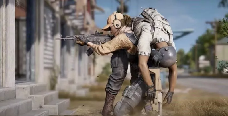 Солдат в PUBG Mobile направляет свое оружие на здание, в то время как она несет еще одного раненого солдата на плечах и спине.