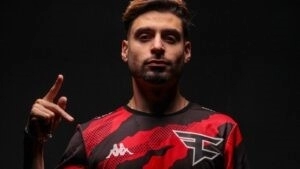 Tommy “ZooMaa” Paparatto holds his hand up in a dark room with a FaZe Clan hand symbol while wearing a FaZe jersey.